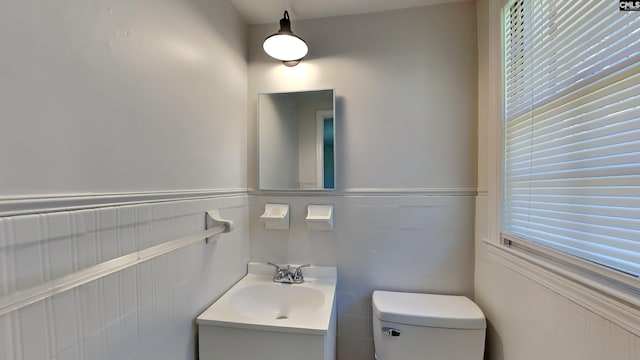 bathroom with vanity, toilet, a healthy amount of sunlight, and a wainscoted wall