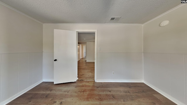 empty room with visible vents, a wainscoted wall, a textured ceiling, and wood finished floors