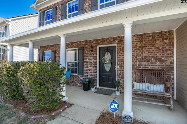 doorway to property with a porch and brick siding