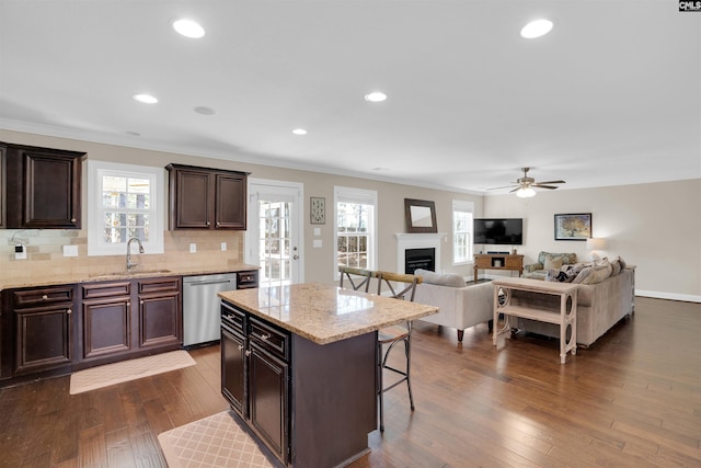 kitchen with a sink, a kitchen breakfast bar, stainless steel dishwasher, a fireplace, and dark wood-style flooring