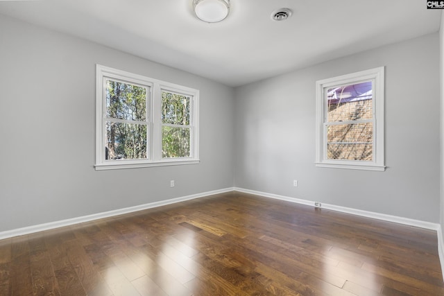 unfurnished room featuring visible vents, baseboards, and dark wood-style floors