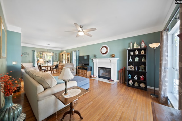 living area with a fireplace with flush hearth, crown molding, a ceiling fan, and wood finished floors