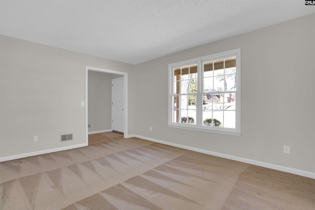 carpeted spare room featuring baseboards, visible vents, and a textured ceiling