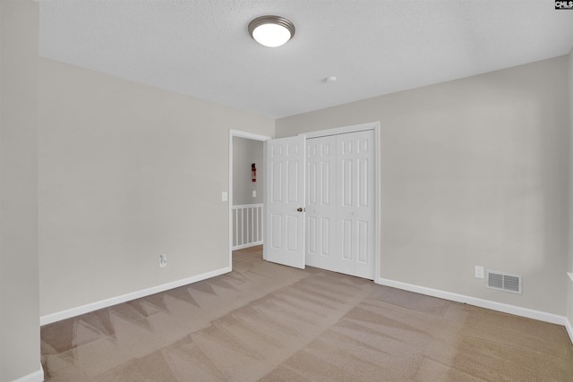 unfurnished bedroom with visible vents, a textured ceiling, a closet, carpet, and baseboards