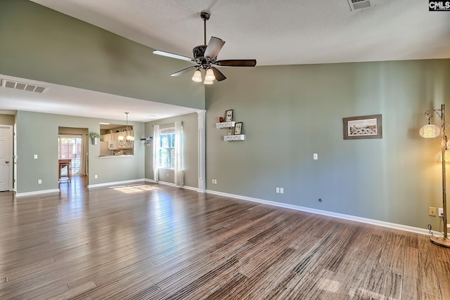 unfurnished living room featuring a wealth of natural light, visible vents, ceiling fan with notable chandelier, and wood finished floors