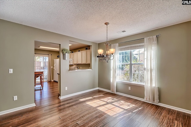 unfurnished dining area with dark wood finished floors, visible vents, a healthy amount of sunlight, and a notable chandelier