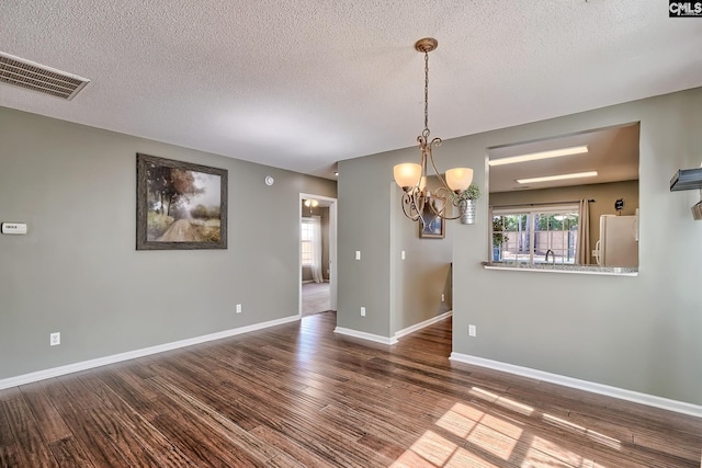 empty room featuring visible vents, baseboards, an inviting chandelier, wood finished floors, and a textured ceiling