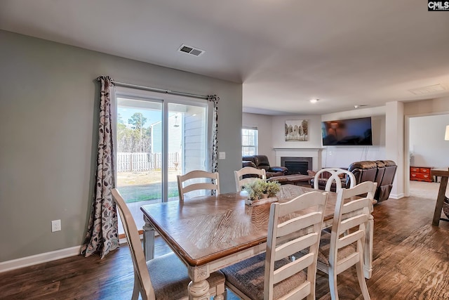 dining room featuring visible vents, baseboards, a glass covered fireplace, and dark wood-style flooring