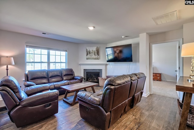 living area featuring visible vents, wood finished floors, baseboards, and a glass covered fireplace