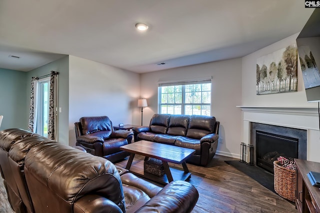 living room featuring visible vents, a fireplace with raised hearth, baseboards, and dark wood-style flooring