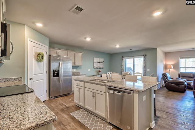 kitchen with visible vents, an island with sink, a sink, wood finished floors, and stainless steel appliances