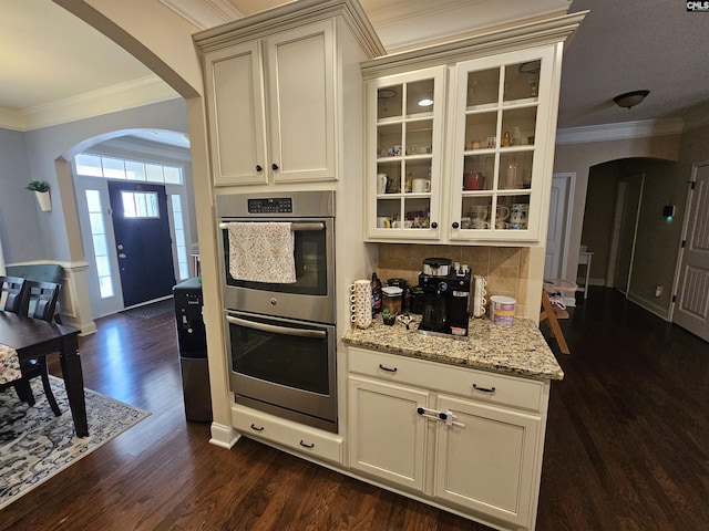 kitchen featuring arched walkways, double oven, dark wood finished floors, and crown molding