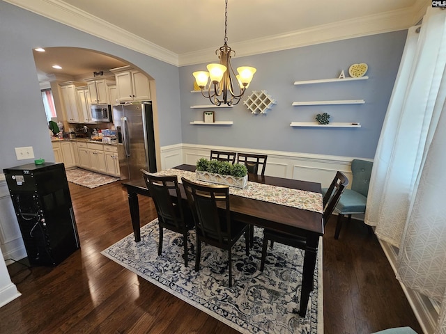 dining space with a wainscoted wall, arched walkways, dark wood finished floors, and ornamental molding