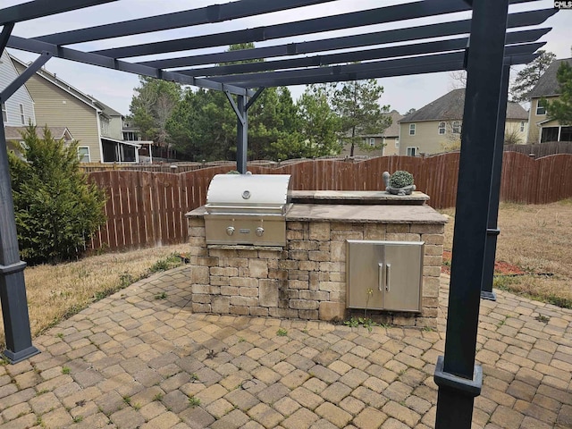 view of patio featuring area for grilling, a fenced backyard, a pergola, and an outdoor kitchen