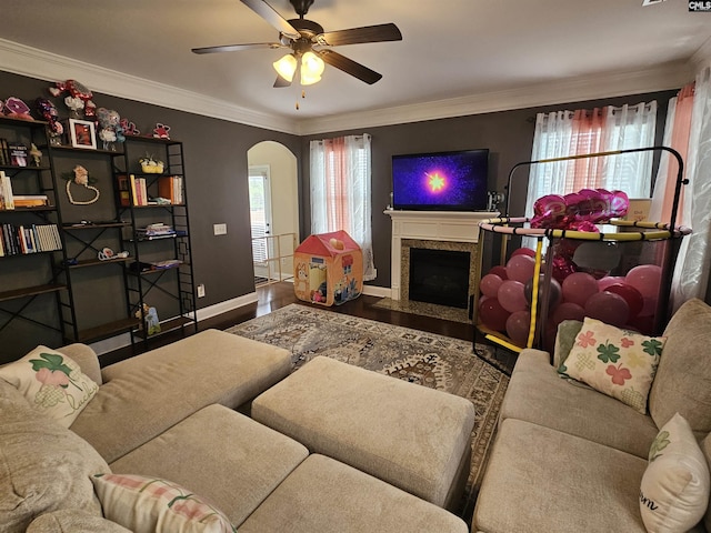 living area featuring wood finished floors, baseboards, a fireplace, arched walkways, and ornamental molding