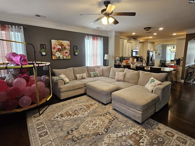 living area featuring visible vents, recessed lighting, dark wood-type flooring, crown molding, and ceiling fan with notable chandelier