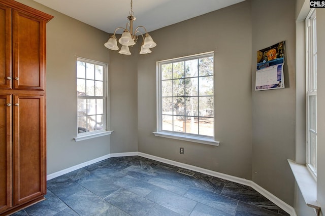 unfurnished dining area with stone finish floor, visible vents, an inviting chandelier, and baseboards