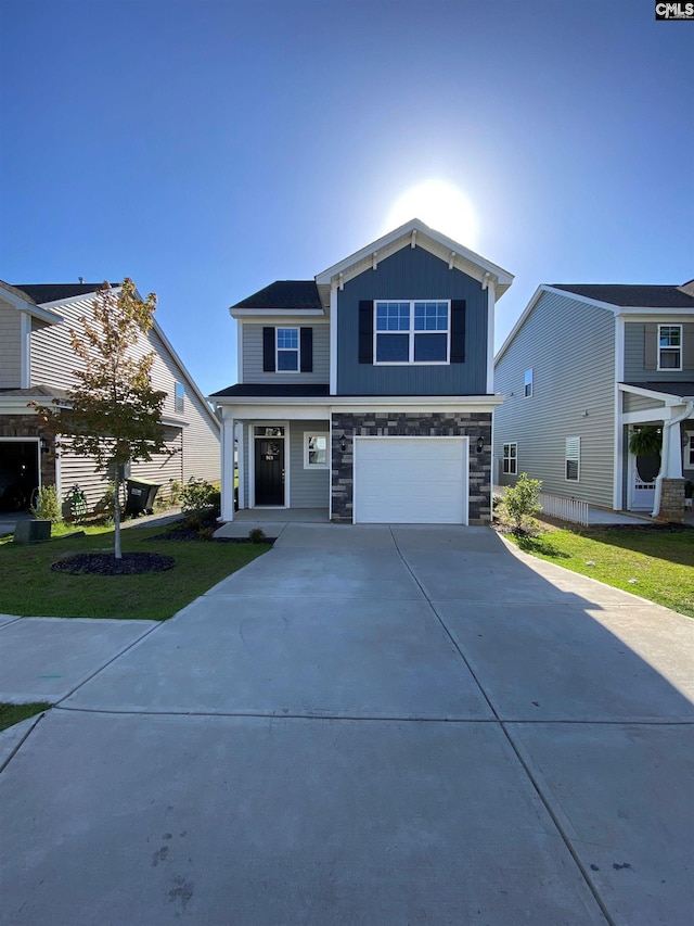 view of front of property featuring board and batten siding, a front yard, a garage, stone siding, and driveway