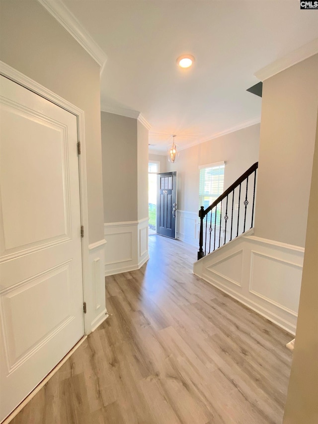 interior space featuring a decorative wall, light wood-style floors, stairs, and crown molding