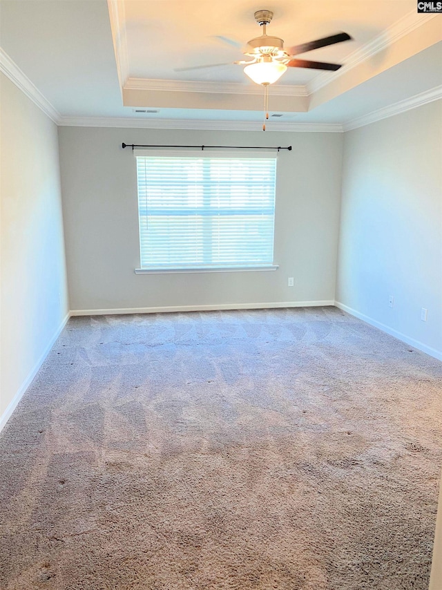 empty room with carpet flooring, a raised ceiling, baseboards, and ornamental molding