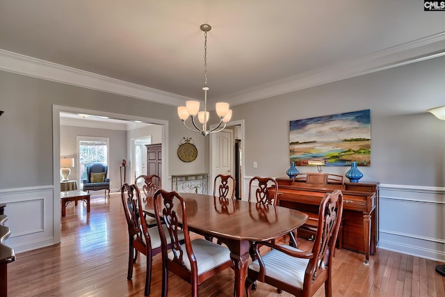 dining room with a notable chandelier, ornamental molding, light wood-style floors, and a wainscoted wall