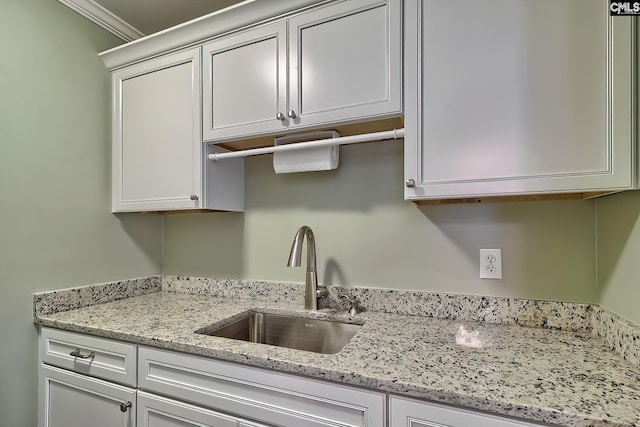 kitchen with white cabinets, light stone countertops, ornamental molding, and a sink