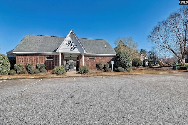 view of front of house featuring brick siding, uncovered parking, a shingled roof, and a playground