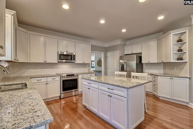 kitchen featuring a kitchen island, crown molding, light wood-style flooring, appliances with stainless steel finishes, and a sink