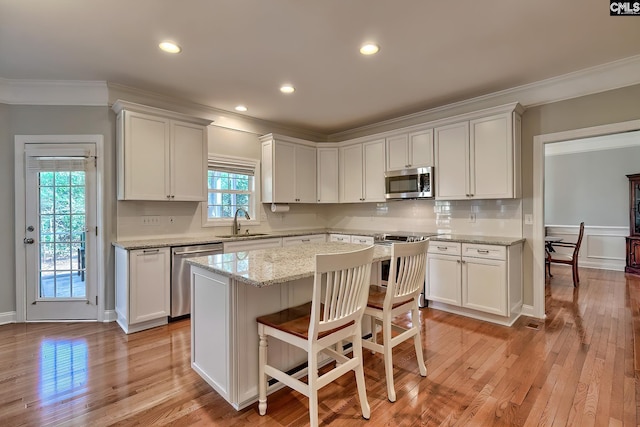 kitchen with a sink, light wood-style flooring, appliances with stainless steel finishes, and ornamental molding