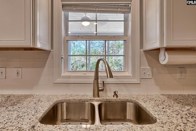 details with white cabinets, light stone counters, backsplash, and a sink