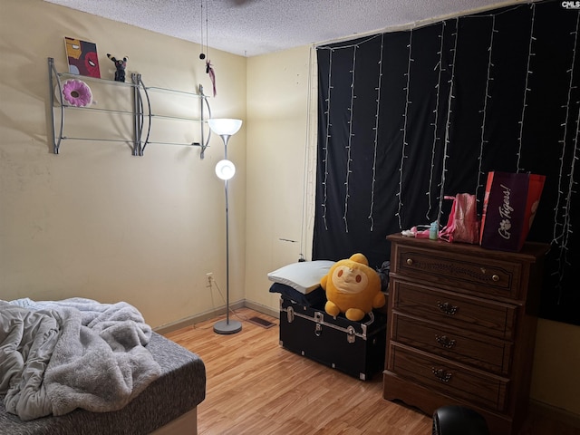 bedroom with light wood-type flooring, baseboards, and a textured ceiling