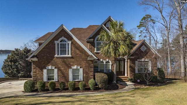 view of front of home featuring brick siding, a water view, a front lawn, and fence