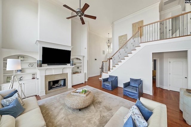 living room with a fireplace with flush hearth, wood finished floors, stairway, a high ceiling, and crown molding