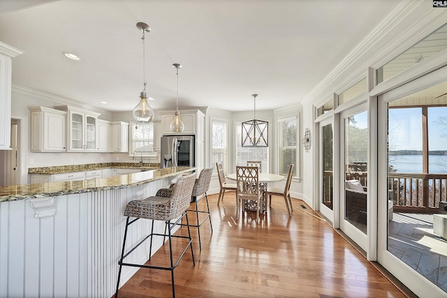 kitchen featuring hardwood / wood-style floors, glass insert cabinets, ornamental molding, and stainless steel refrigerator with ice dispenser