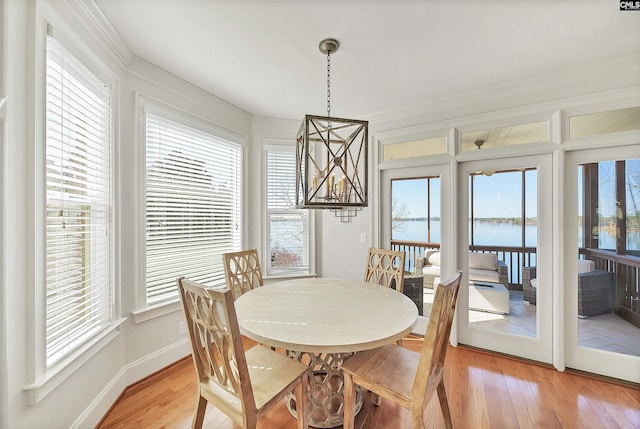 dining room with baseboards, crown molding, light wood-style floors, and a water view