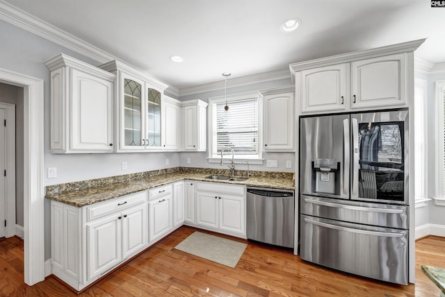 kitchen featuring dark stone countertops, light wood finished floors, a sink, stainless steel appliances, and white cabinets