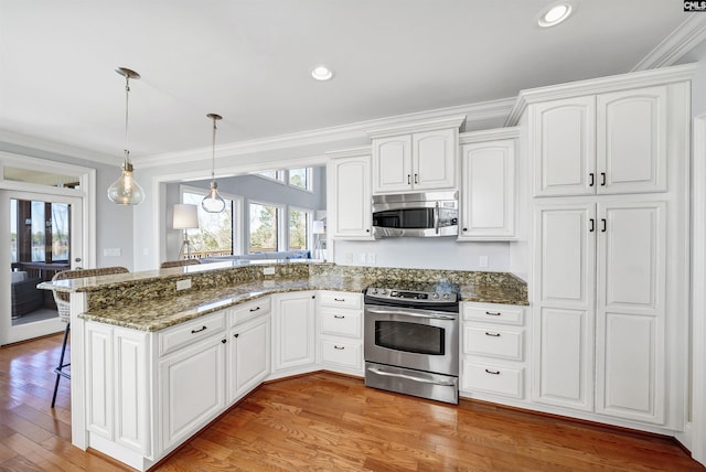 kitchen featuring dark stone countertops, a kitchen breakfast bar, stainless steel appliances, a peninsula, and light wood finished floors