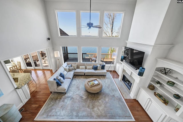 living area with a ceiling fan, dark wood-type flooring, a high ceiling, and a fireplace