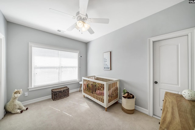 bedroom featuring a nursery area, ceiling fan, baseboards, and carpet floors