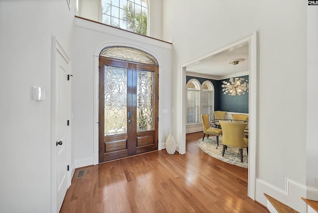 entryway with visible vents, baseboards, an inviting chandelier, a towering ceiling, and wood-type flooring