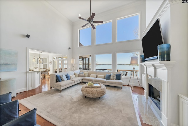 living area featuring a ceiling fan, wood finished floors, baseboards, a premium fireplace, and ornamental molding