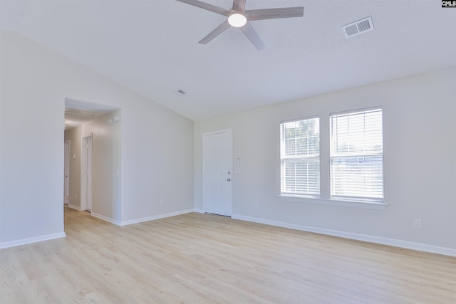 spare room featuring light wood finished floors, visible vents, baseboards, and lofted ceiling