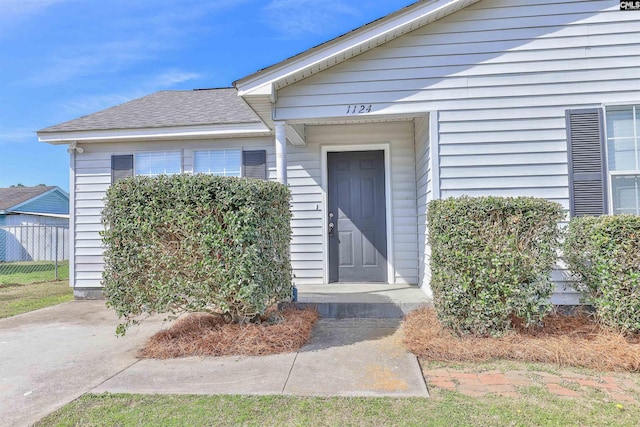 property entrance with a shingled roof and fence