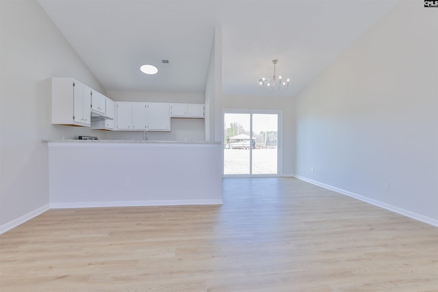 kitchen featuring vaulted ceiling, white cabinets, a notable chandelier, and light wood-style floors