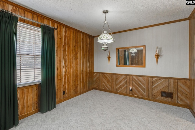 empty room featuring visible vents, wood walls, ornamental molding, carpet floors, and a textured ceiling