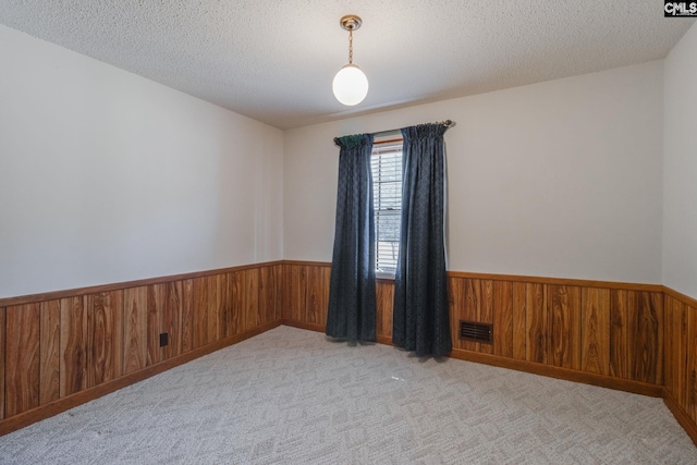 carpeted spare room featuring a textured ceiling, wooden walls, visible vents, and wainscoting