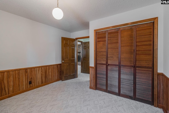 unfurnished bedroom featuring a textured ceiling, a closet, wood walls, wainscoting, and light colored carpet