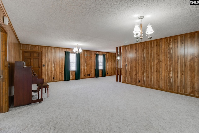 interior space with light carpet, a notable chandelier, wood walls, and a textured ceiling