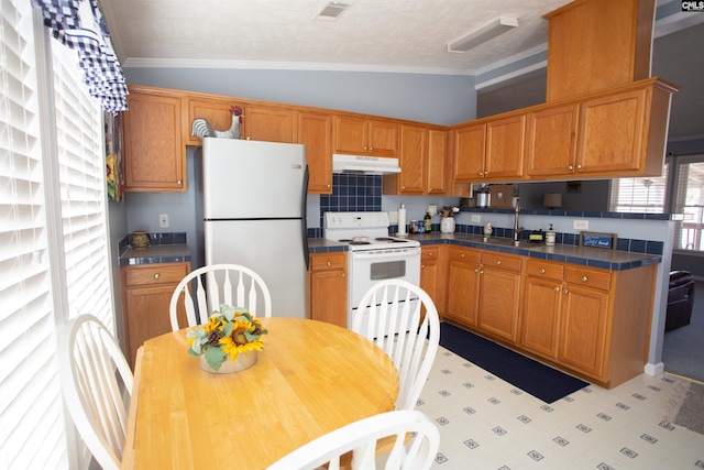 kitchen with under cabinet range hood, tile countertops, white appliances, and crown molding