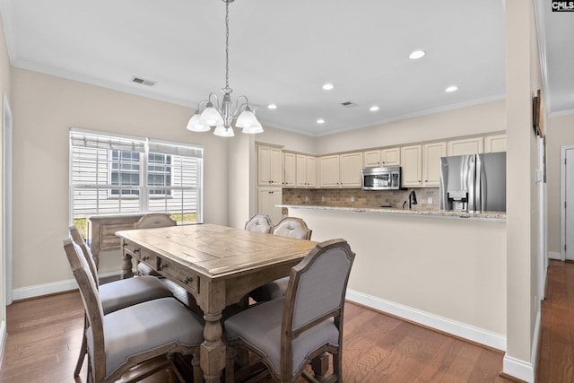 dining space featuring visible vents, crown molding, an inviting chandelier, and wood finished floors